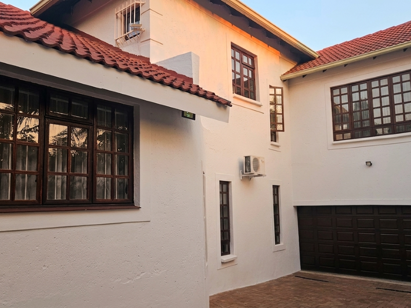 A well-maintained exterior view of the property featuring white rendered walls, terracotta roof tiles, timber-framed windows, and a paved driveway with garage access.