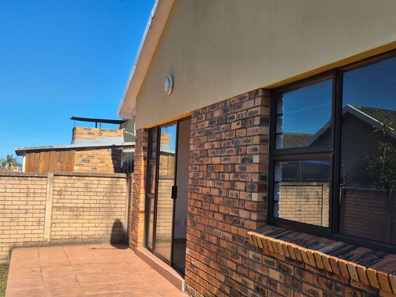 Rear view of the townhouse featuring a paved patio area, face-brick exterior walls, and aluminium-framed sliding doors leading into the home.