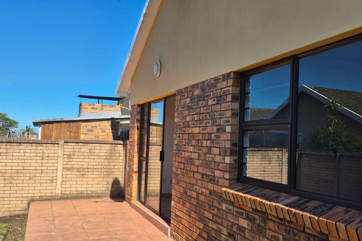 Rear view of the townhouse featuring a paved patio area, face-brick exterior walls, and aluminium-framed sliding doors leading into the home.