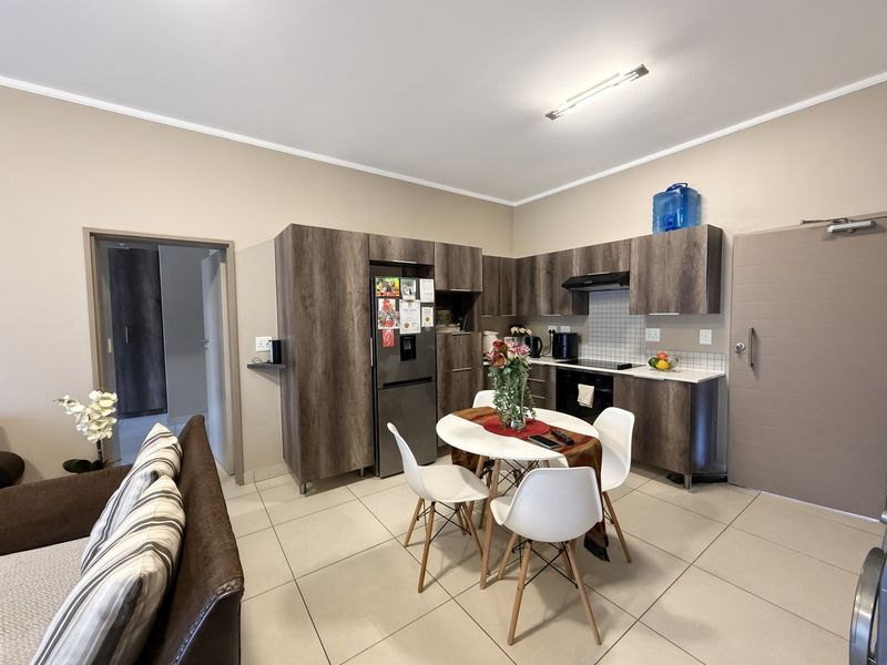 An open-plan living and kitchen area featuring modern wood-finish cabinetry, tiled flooring, and integrated kitchen appliances in a well-maintained apartment setting.