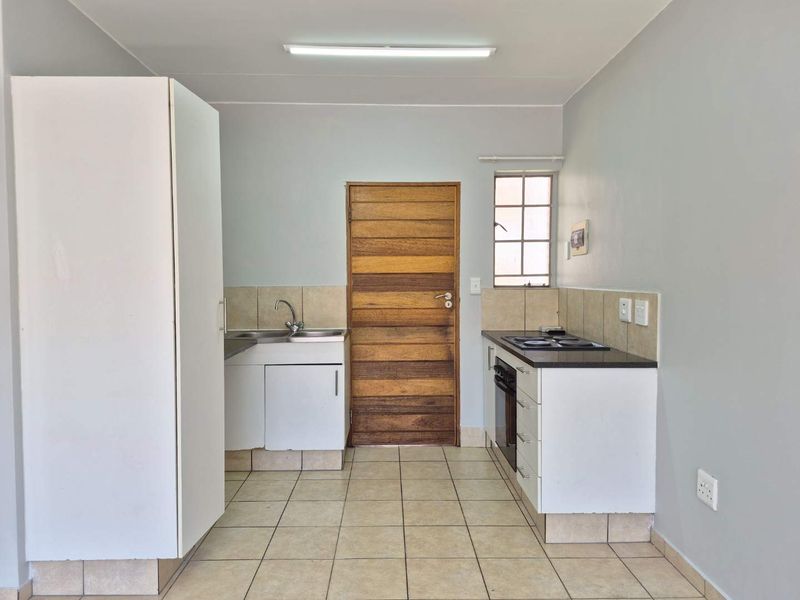 A functional, empty kitchen featuring built-in cabinetry, a stainless steel sink, an integrated oven and hob, and tiled flooring.