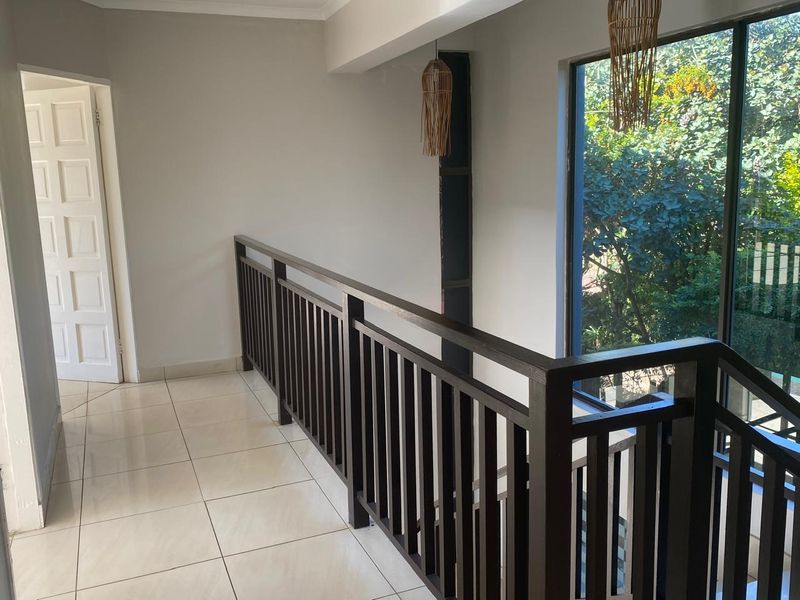 A bright upstairs landing area featuring tiled flooring, a dark timber balustrade, and large windows overlooking the garden.
