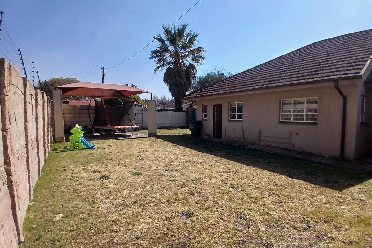 Rear exterior view of the property featuring a lawn, a covered patio area, and a secure boundary wall.
