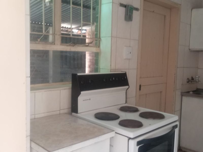 A dated kitchen featuring tiled walls, built-in cabinetry, and a freestanding stove, offering potential for modernization and renovation.