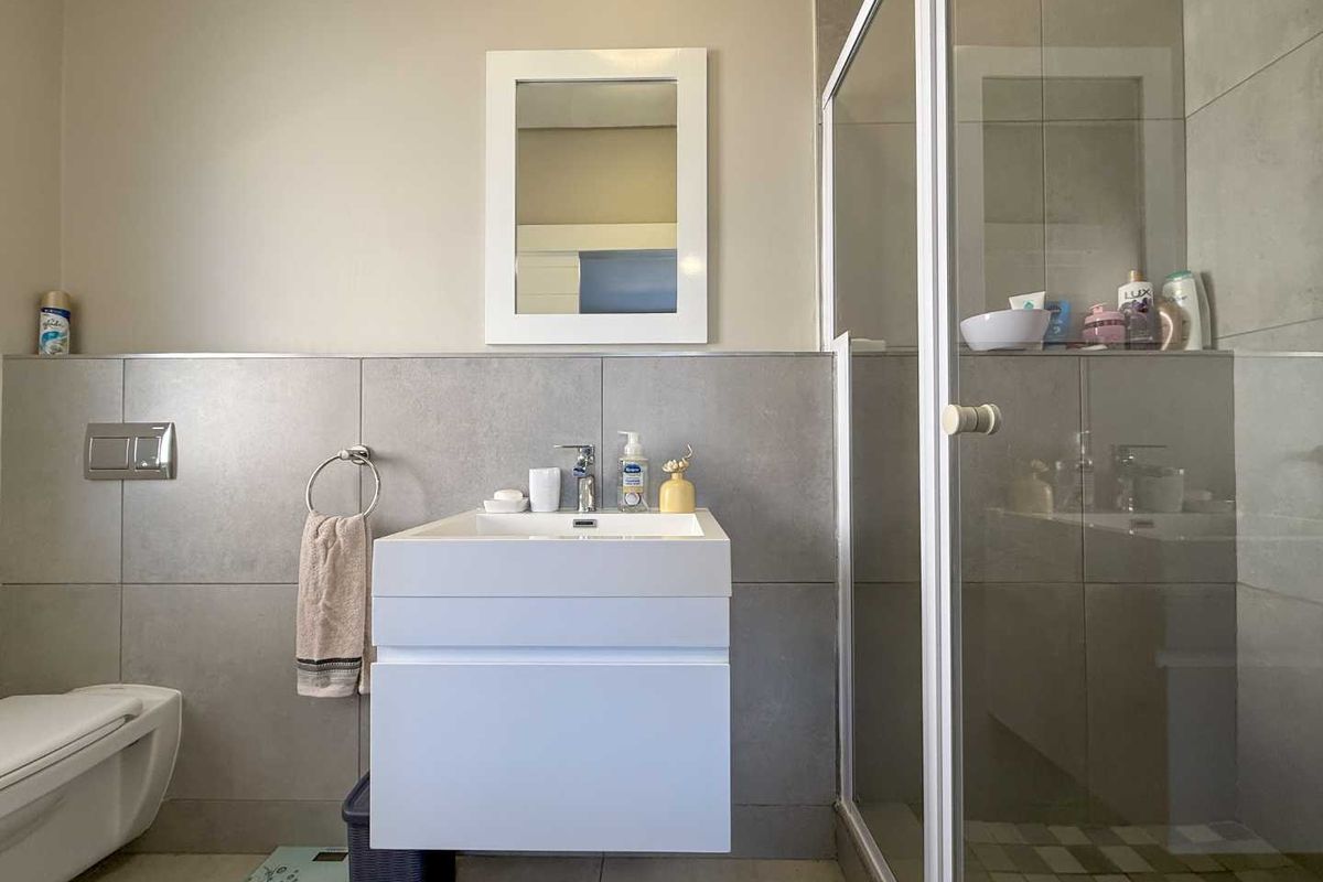 Modern bathroom featuring a wall-mounted vanity, a glass-enclosed shower, and a wall-hung toilet with neutral grey tiling.