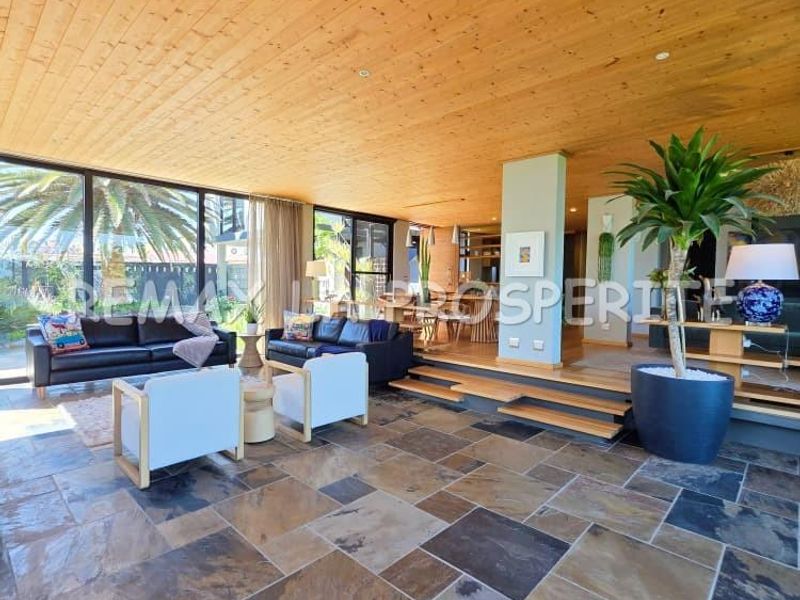 Spacious open-plan living area featuring natural slate flooring, a warm timber-clad ceiling, and expansive floor-to-ceiling glass doors leading to the exterior.