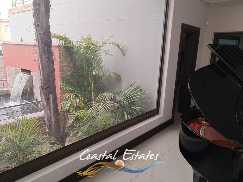 A bright living area featuring large windows with a view of an outdoor water feature and landscaped garden.