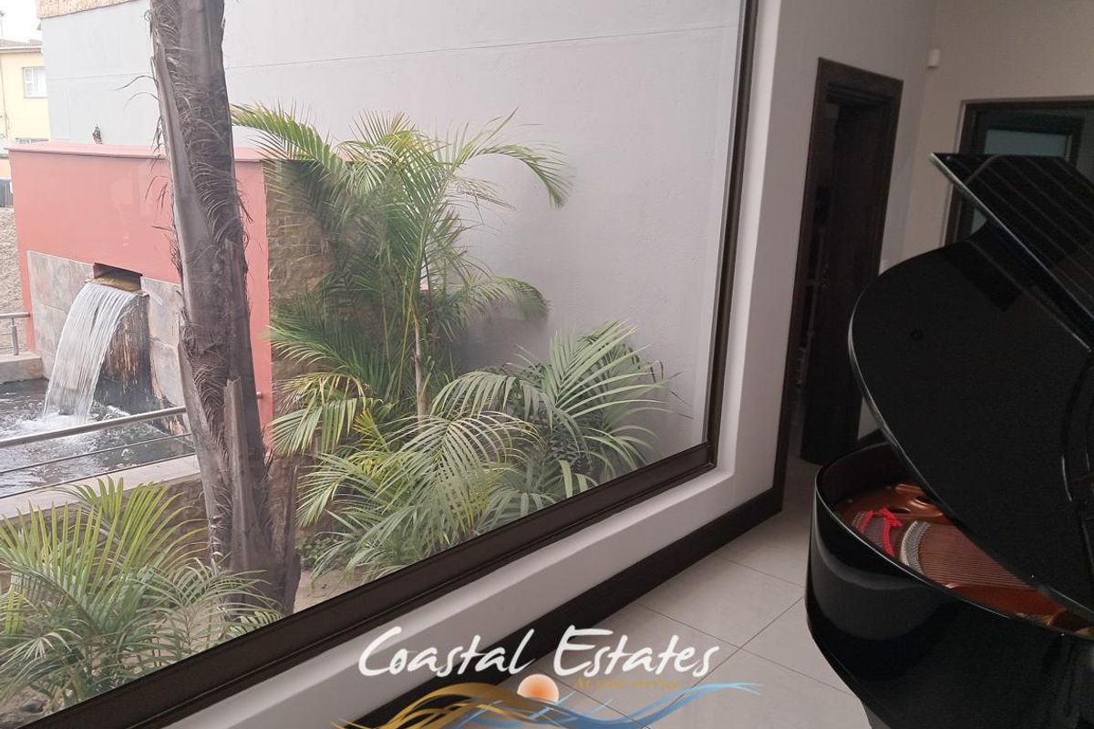 A bright living area featuring large windows with a view of an outdoor water feature and landscaped garden.