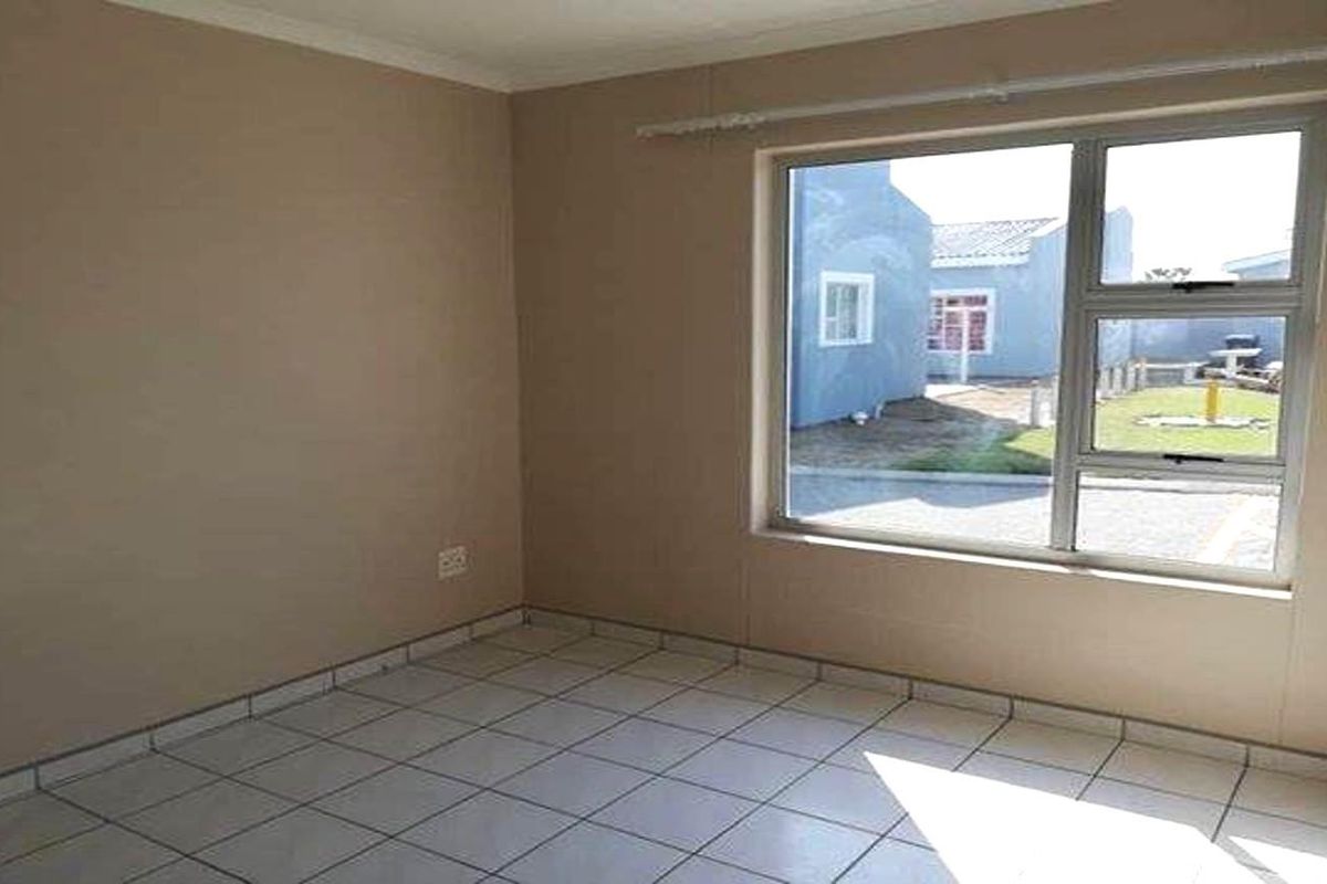 A vacant bedroom featuring neutral wall paint, tiled flooring, and a large window providing natural light and a view of the exterior.