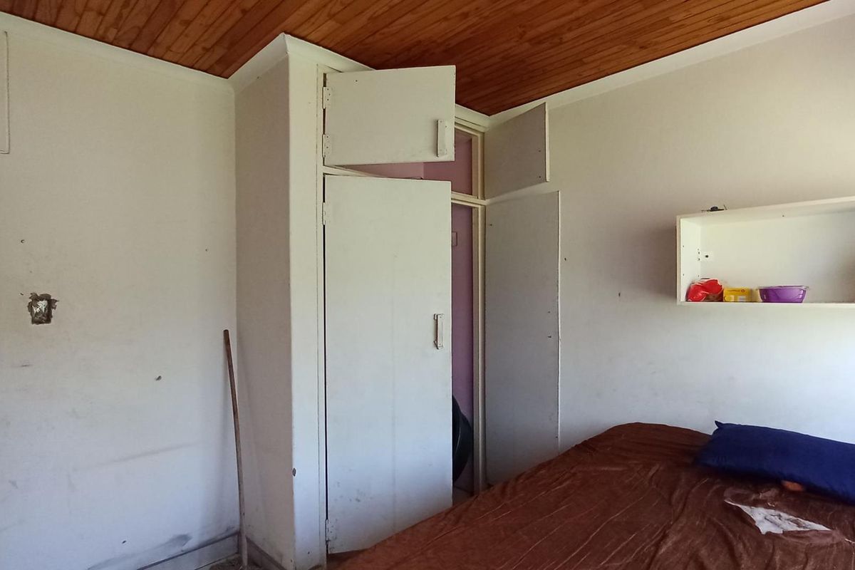 A bedroom featuring a wooden ceiling, built-in cupboards, and a wall-mounted shelf, requiring cosmetic updates to improve its overall condition.