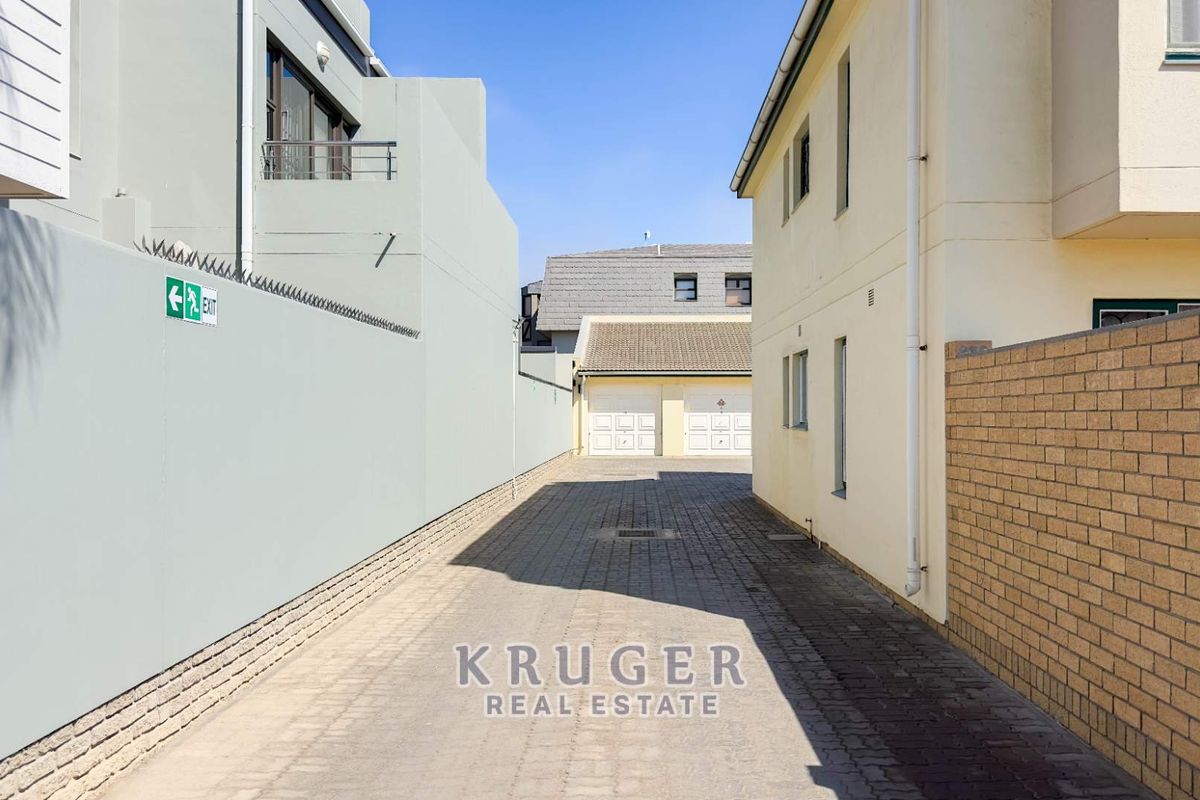 A paved driveway leading to a double garage, flanked by boundary walls and residential building facades.