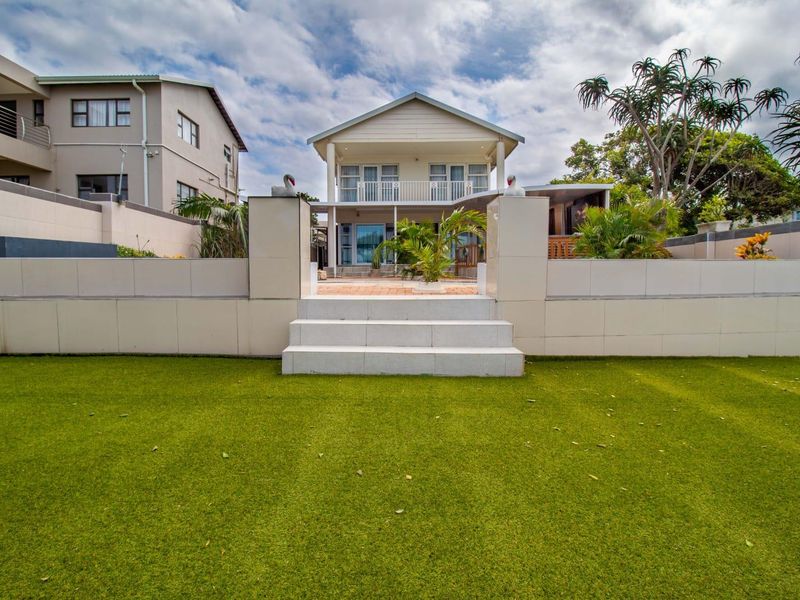 Rear view of the townhouse featuring a landscaped artificial lawn, tiled retaining wall with stairs, and an upper-level balcony.