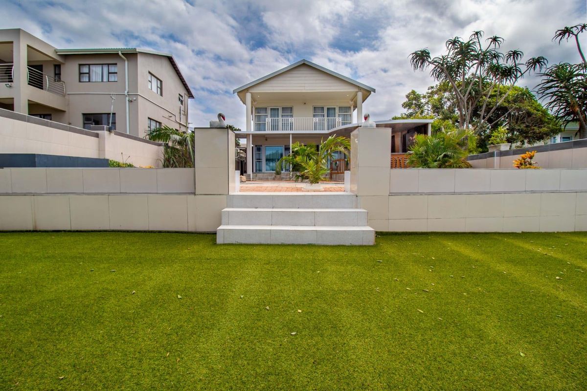 Rear view of the townhouse featuring a landscaped artificial lawn, tiled retaining wall with stairs, and an upper-level balcony.