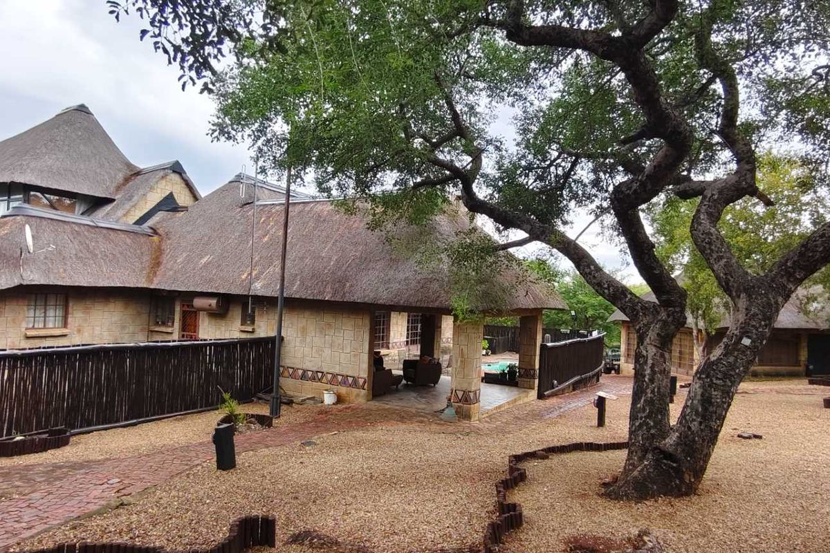 Rear view of a stone-clad house featuring a traditional thatch roof, a covered patio area, and established garden surroundings.