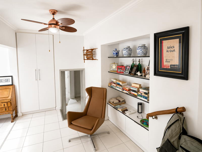 A bright living area featuring tiled floors, built-in storage cupboards, recessed shelving, and a modern ceiling fan, providing a clean and functional space.