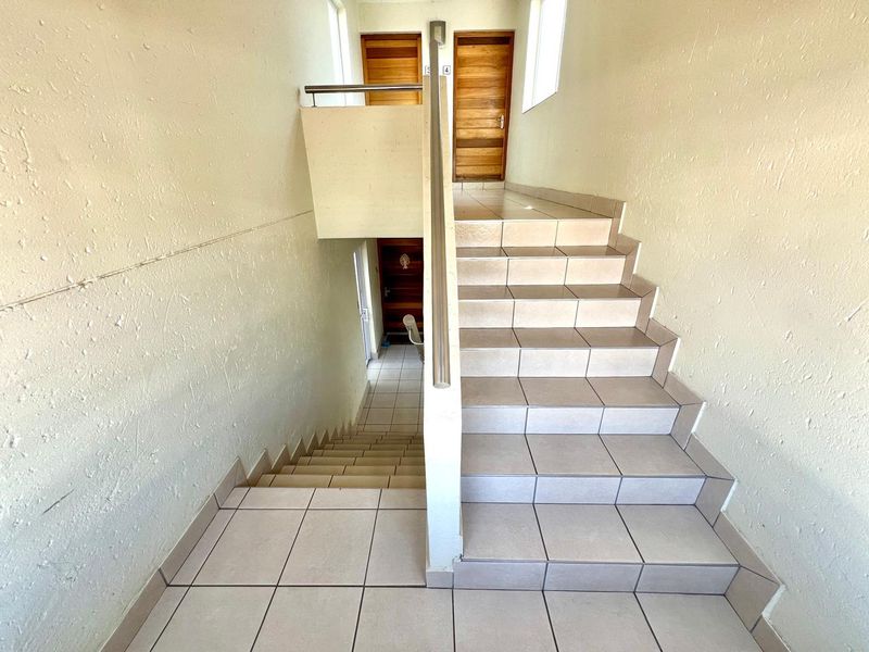 A functional apartment stairwell featuring tiled steps, a metal handrail, and access to multiple wooden entry doors.