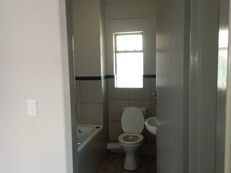 A functional bathroom featuring a toilet, bathtub, and washbasin with tiled flooring and wall accents, viewed from the adjacent hallway.