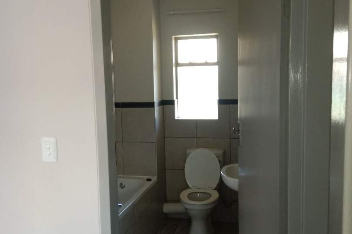 A functional bathroom featuring a toilet, bathtub, and washbasin with tiled flooring and wall accents, viewed from the adjacent hallway.