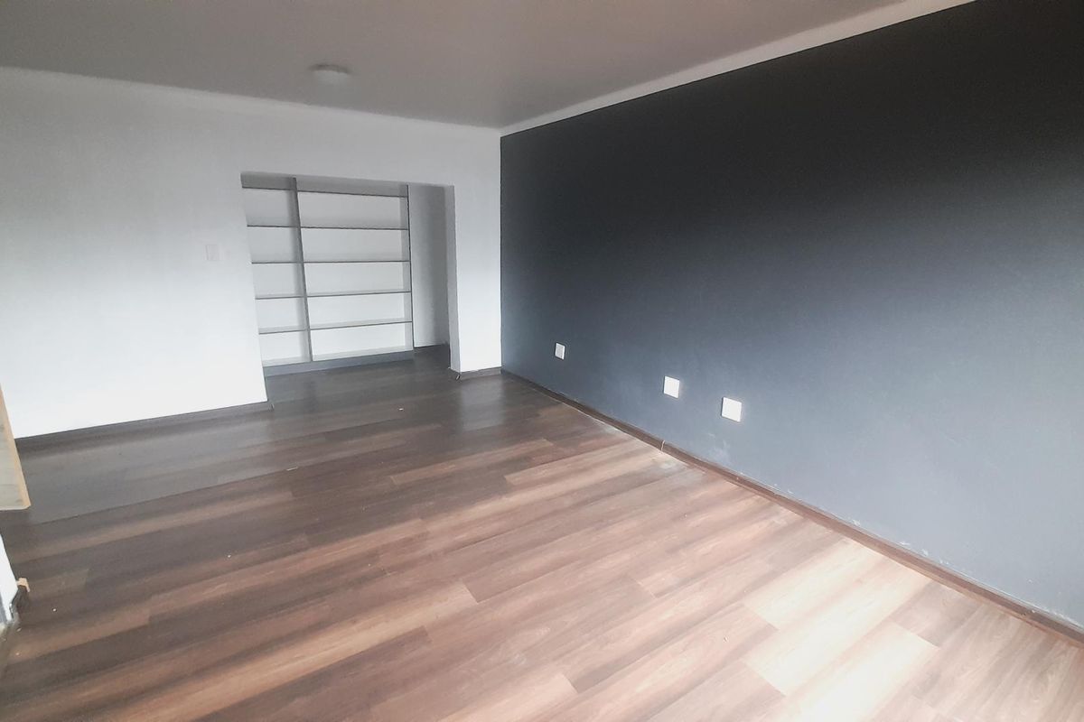 An empty living room featuring dark wood-look laminate flooring, a charcoal accent wall, and a recessed alcove with built-in shelving.