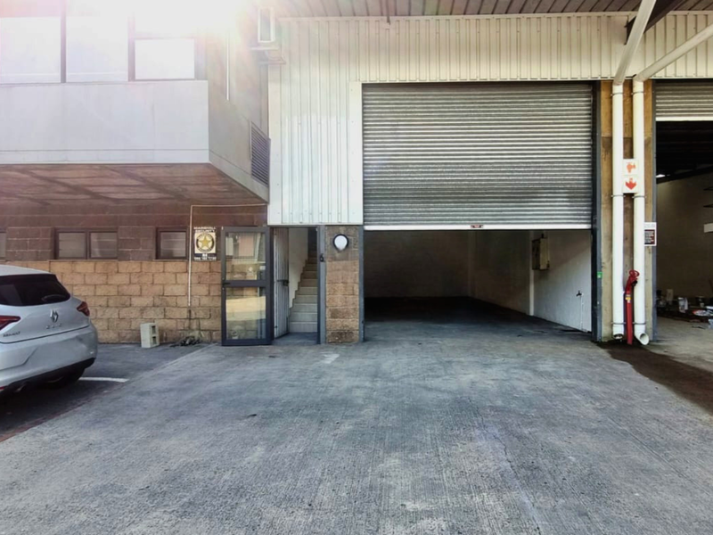 Industrial unit exterior featuring a large roller shutter door, concrete driveway, and external staircase access.