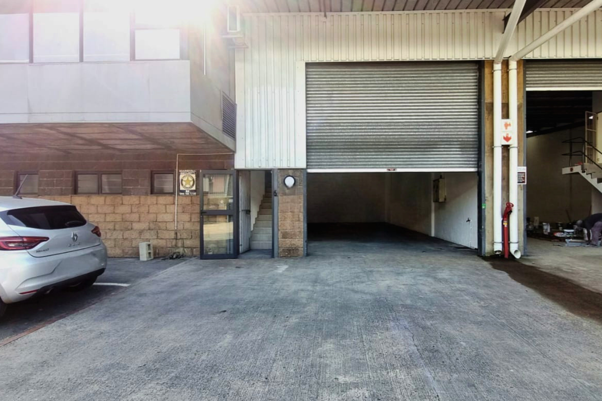 Industrial unit exterior featuring a large roller shutter door, concrete driveway, and external staircase access.