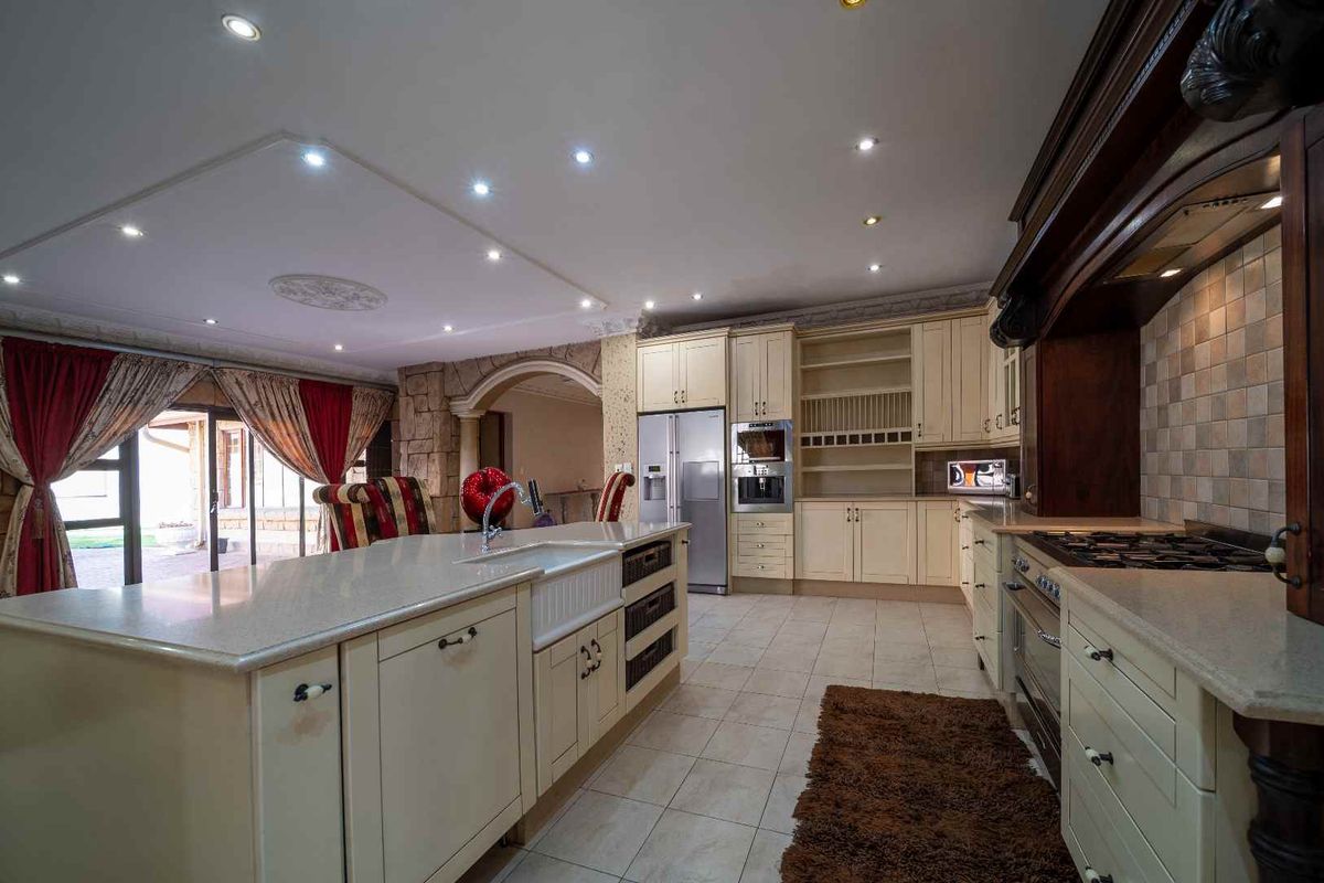 Spacious kitchen featuring a large central island with a farmhouse sink, stone countertops, built-in oven, and integrated cabinetry with recessed lighting.