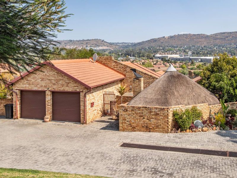 Front exterior view of a townhouse featuring a double garage, brick facade, and a unique thatched roof section with a paved driveway.