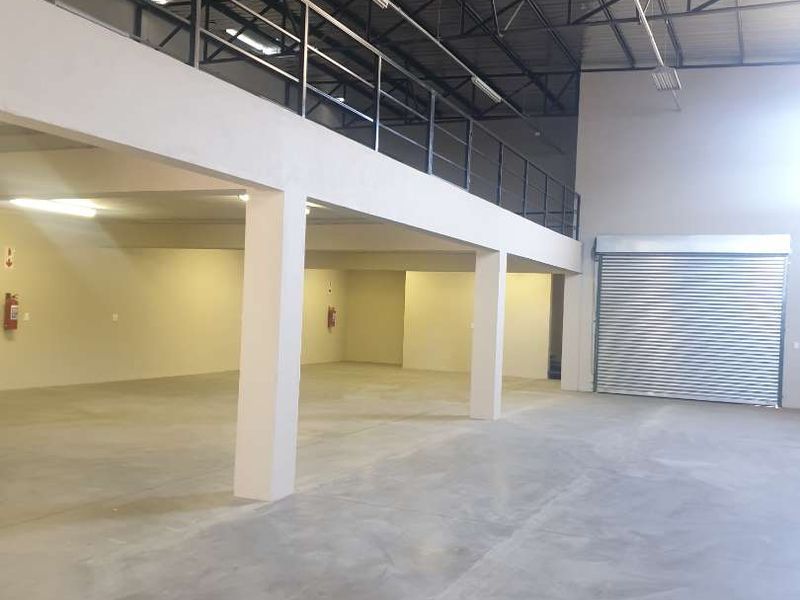 Spacious industrial warehouse unit featuring a mezzanine level, concrete flooring, exposed steel roof trusses, and a large roller shutter door for easy access.