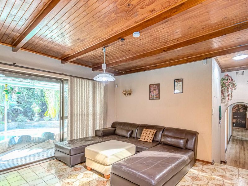 Living room featuring a warm timber-clad ceiling with exposed beams, tiled flooring, and a sliding glass door providing access to the outdoor area.