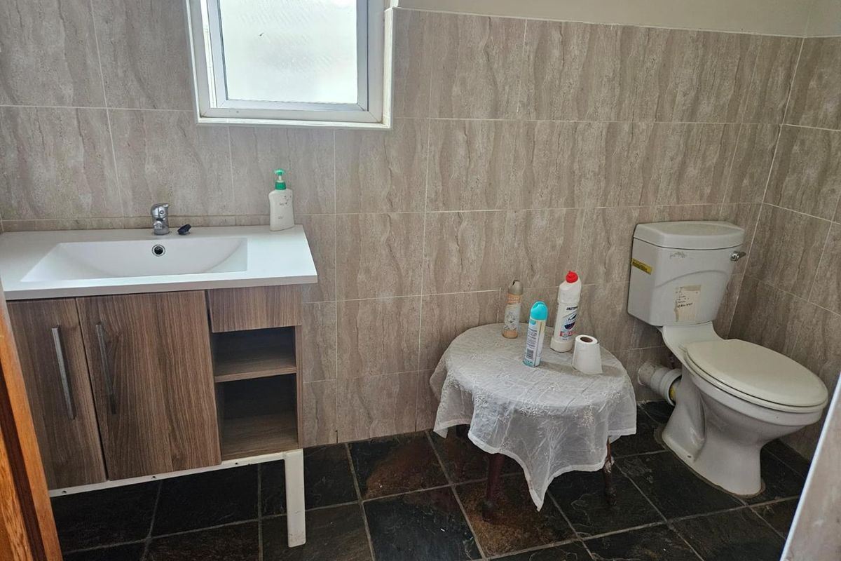 A functional bathroom featuring a modern vanity unit with integrated basin, a standard toilet, and neutral wall tiling.