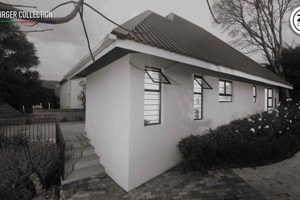Rear exterior view of the property featuring a corrugated metal roof, paved pathways, and concrete stairs with metal railings.