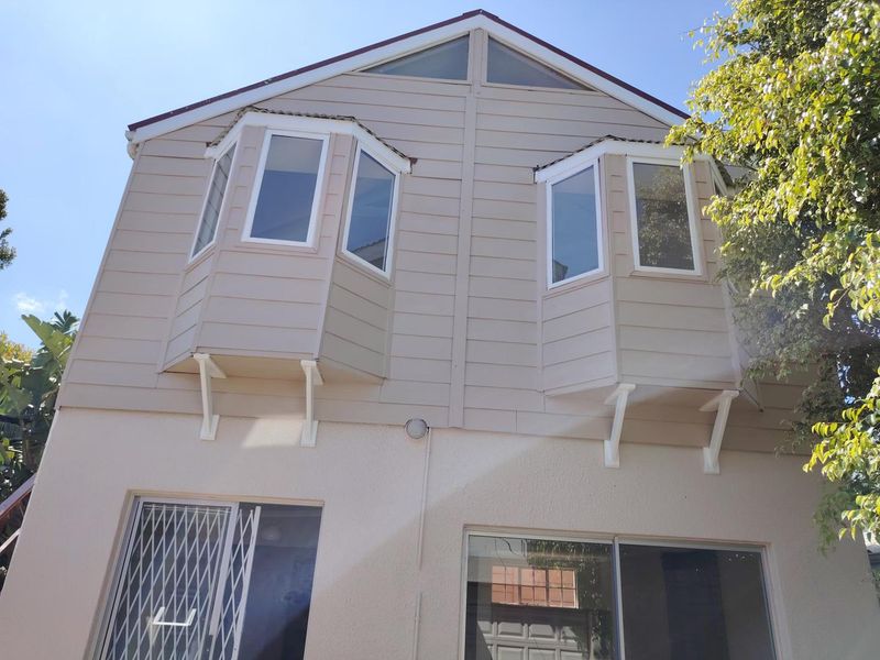 Rear elevation of the cottage featuring dual bay windows, sliding glass doors with security gate, and well-maintained exterior cladding.