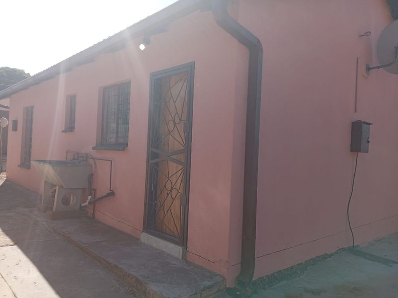 Rear exterior view of the house featuring a security gate, external laundry sink, and basic utility fixtures against a pink rendered wall.