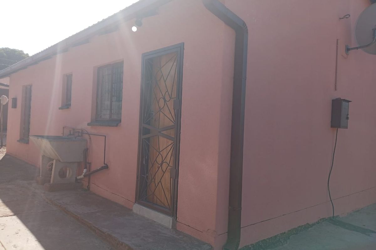 Rear exterior view of the house featuring a security gate, external laundry sink, and basic utility fixtures against a pink rendered wall.