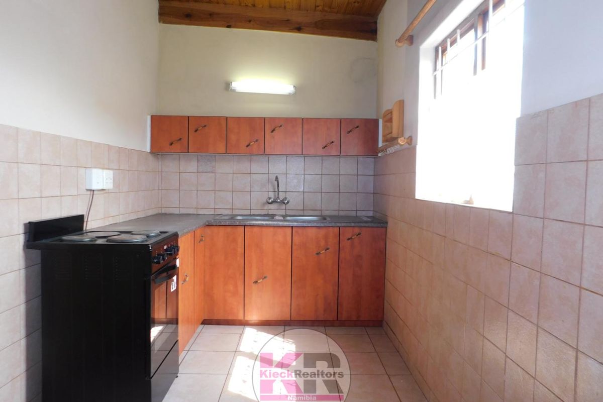 A functional kitchen featuring wooden cabinetry, tiled splashbacks, a double sink, and a freestanding stove under a timber-paneled ceiling.