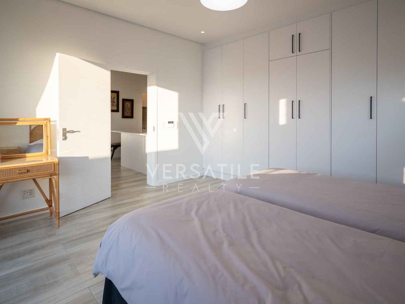 A bright, modern bedroom featuring extensive floor-to-ceiling built-in cupboards and light-toned laminate flooring.