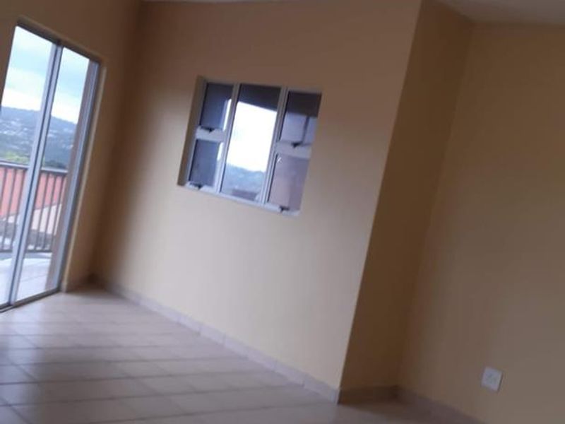An empty, neutrally painted living room featuring tiled flooring, a sliding glass door leading to a balcony, and natural light from multiple windows.