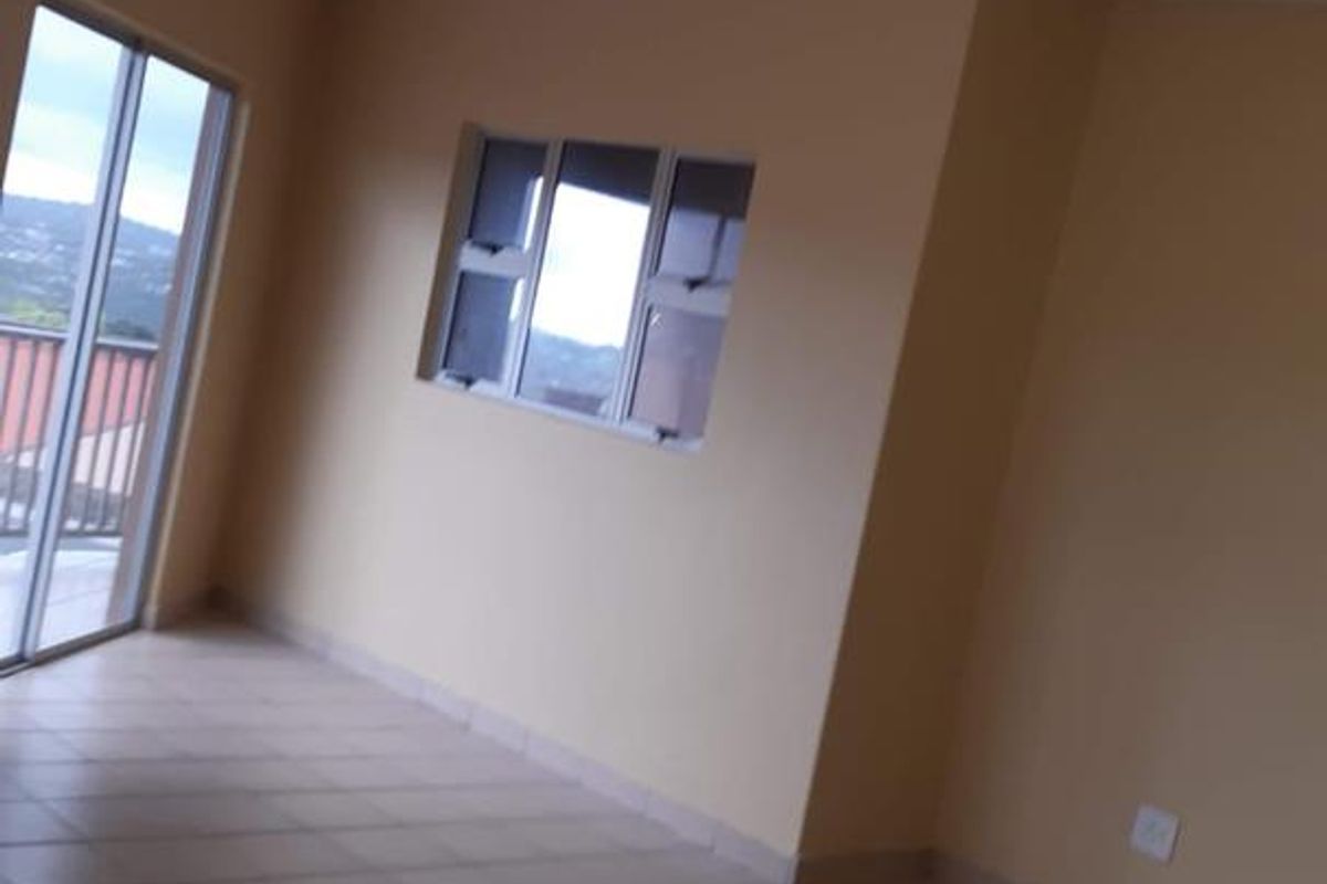 An empty, neutrally painted living room featuring tiled flooring, a sliding glass door leading to a balcony, and natural light from multiple windows.