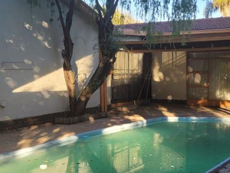 Outdoor pool area featuring a swimming pool, paved patio, and covered patio space, requiring maintenance and cleaning.