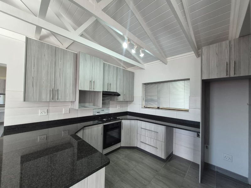 Modern kitchen featuring granite countertops, built-in oven, gas hob, extractor fan, and light timber-look cabinetry under an exposed beam ceiling.