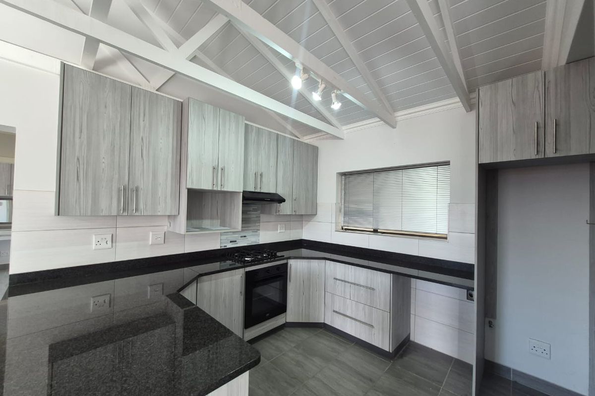 Modern kitchen featuring granite countertops, built-in oven, gas hob, extractor fan, and light timber-look cabinetry under an exposed beam ceiling.