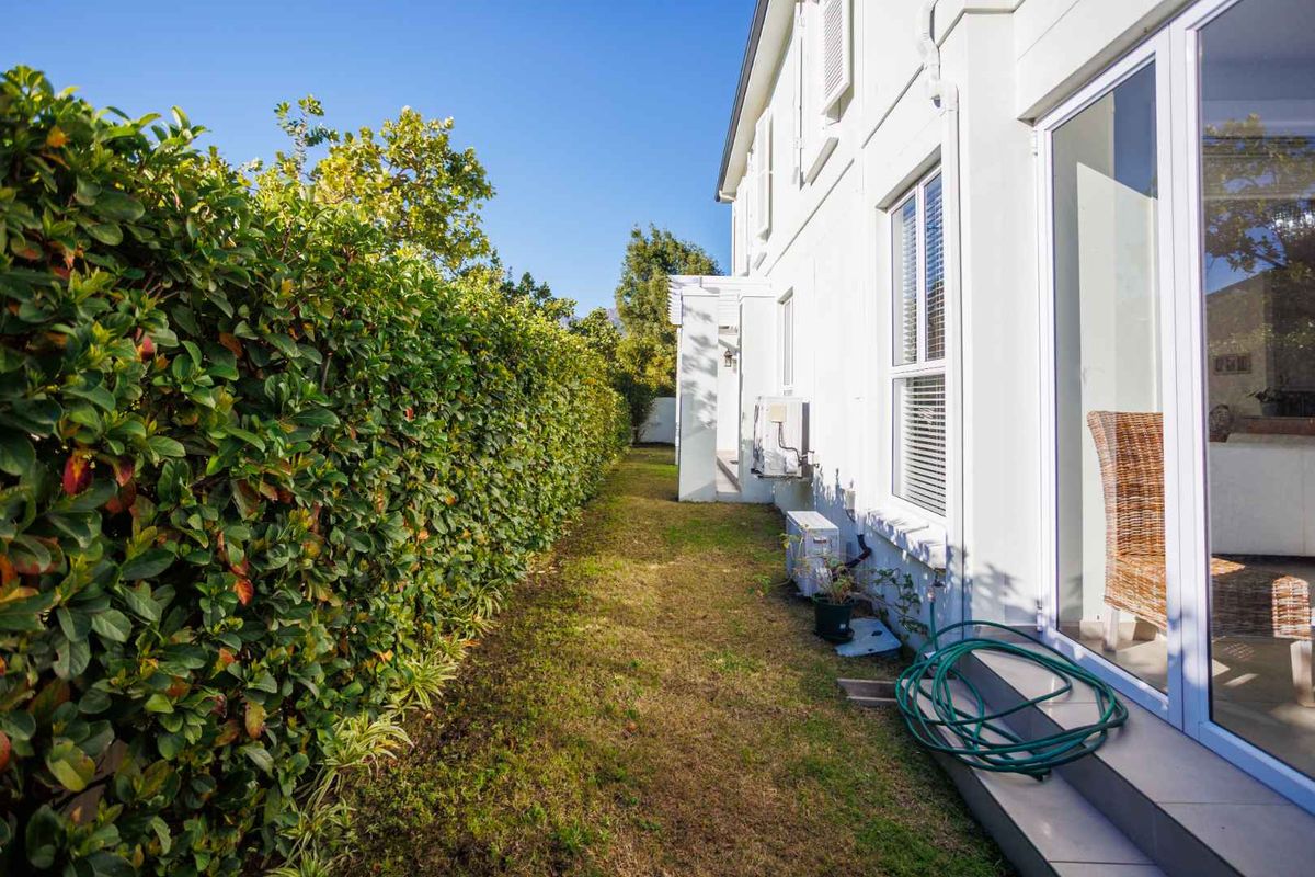 A side garden pathway featuring a manicured hedge, tiled patio threshold, and exterior wall access with sliding glass doors.