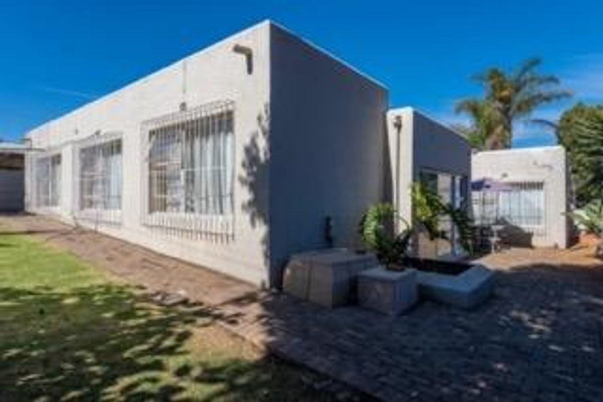Rear exterior view of the house featuring a paved patio area, lawn, and security bars on the windows.