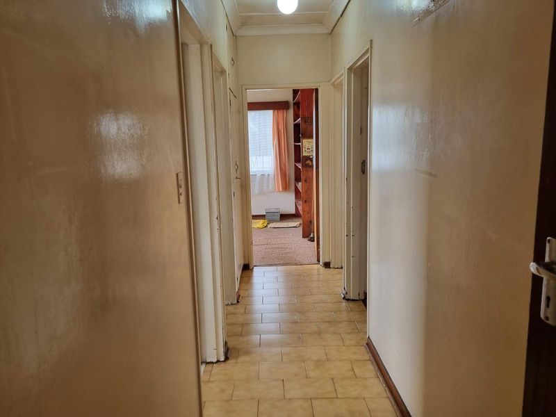 A functional hallway featuring tiled flooring and access to multiple rooms, showing signs of wear and dated finishes.