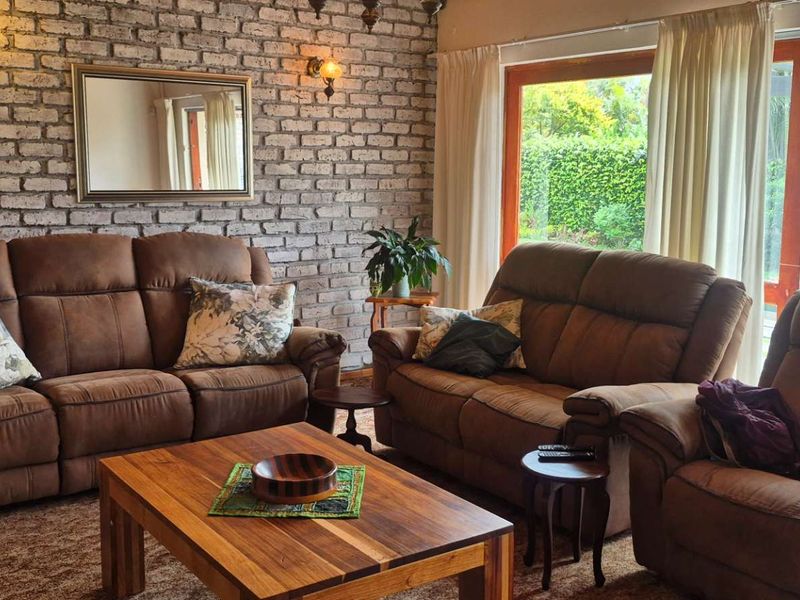 A cozy living room featuring an exposed brick feature wall, warm lighting, and large sliding glass doors providing natural light and garden views.