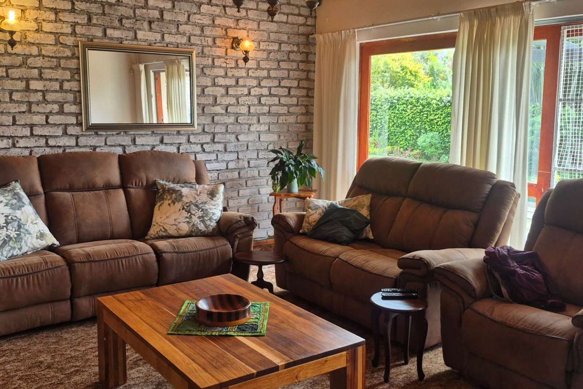 A cozy living room featuring an exposed brick feature wall, warm lighting, and large sliding glass doors providing natural light and garden views.