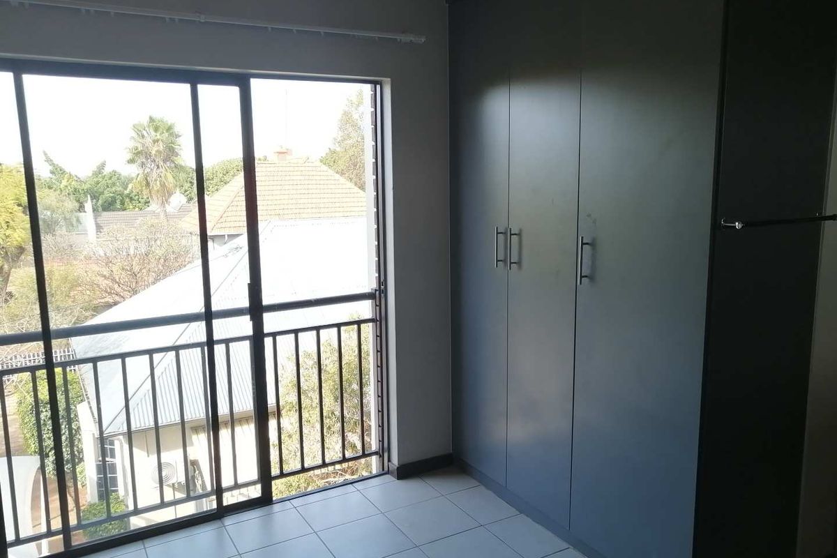 A bright, empty bedroom featuring modern dark grey built-in cupboards, tiled flooring, and a sliding glass door leading to a balcony.