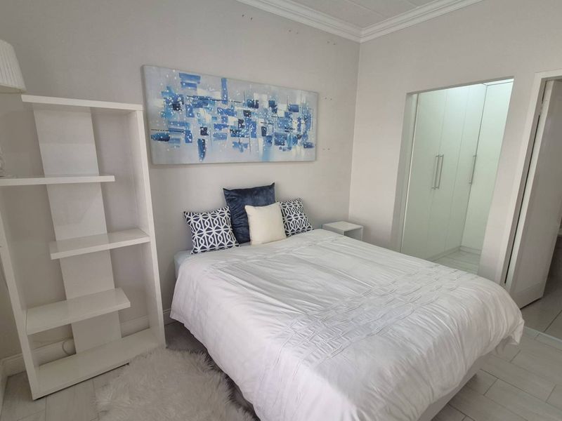 A well-maintained bedroom featuring neutral tiled flooring, decorative cornicing, and convenient built-in cupboards with an adjoining en-suite bathroom.