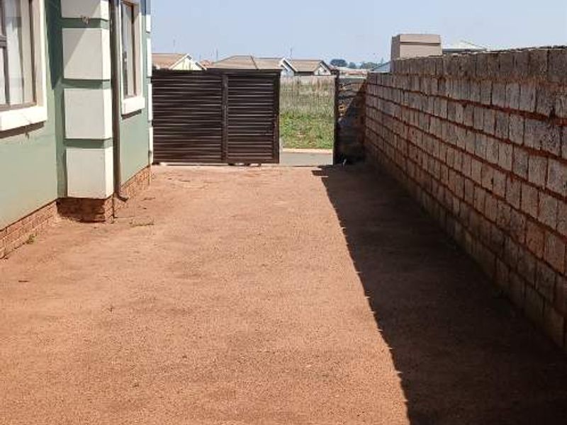 A side or rear exterior view of the property featuring a brick boundary wall, metal gate, and unpaved ground area.