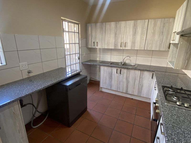 A functional kitchen featuring granite countertops, built-in cabinetry, a gas hob with extractor, and tiled flooring with direct access to the exterior.